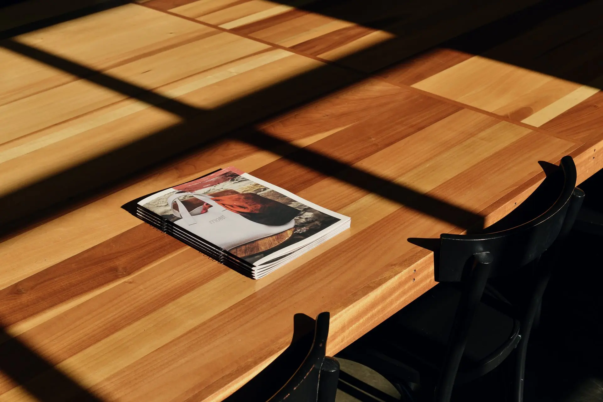Des magazines sur une table de studio en bois, dans la lumière rasante du soleil.