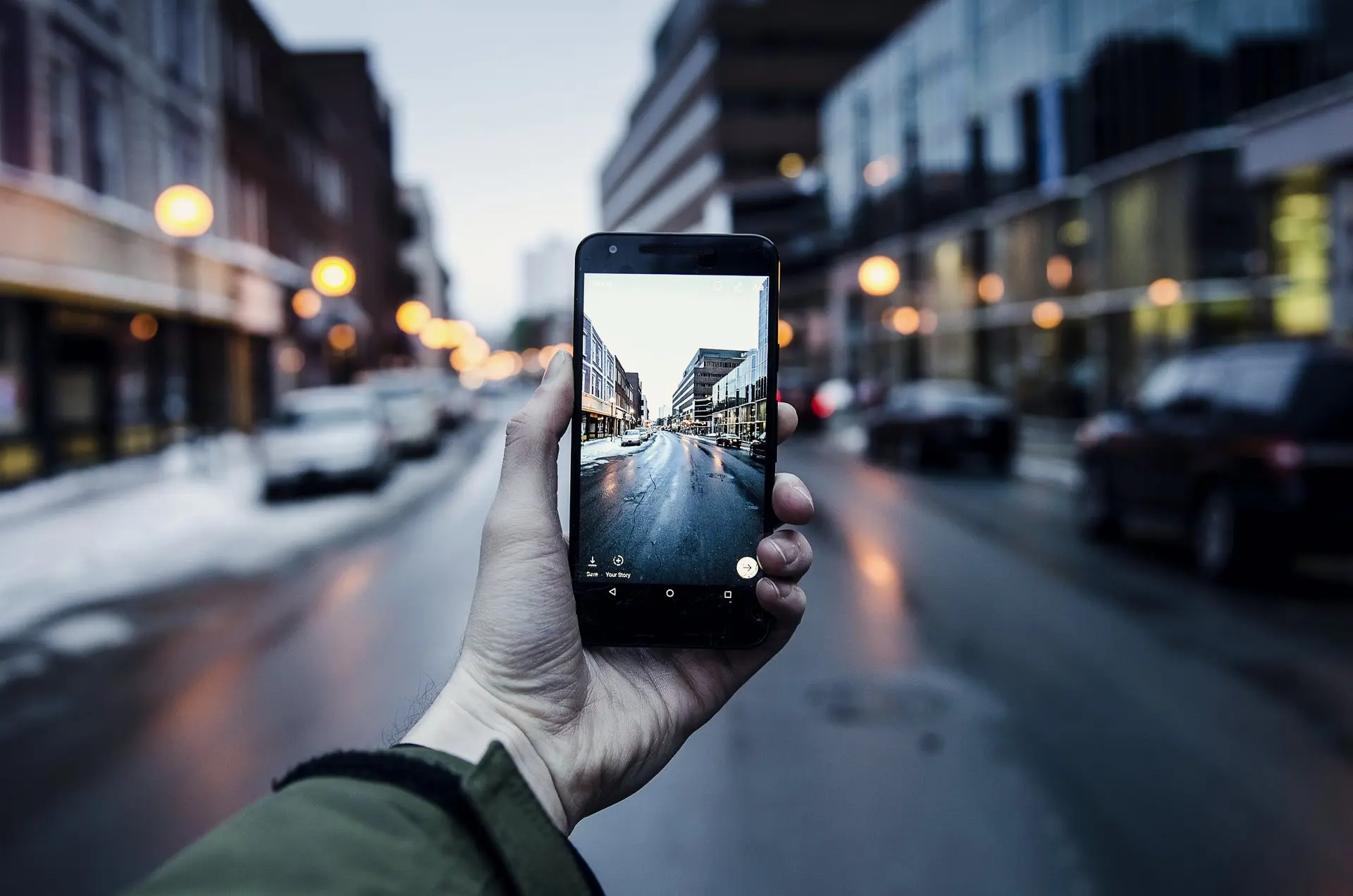 Une main filme une rue en ville à l’aube avec un téléphone.