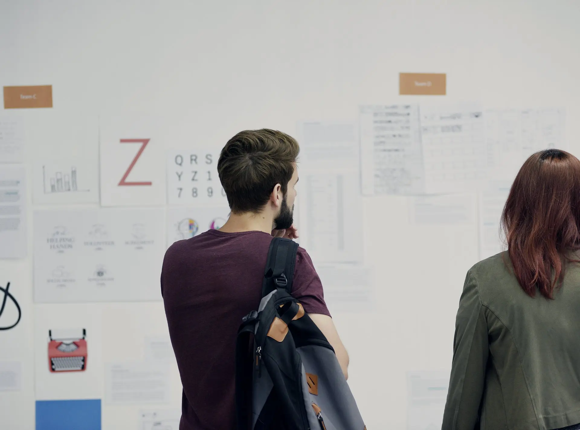 Deux personnes examinent des maquettes imprimées, épinglées au mur d’un studio.