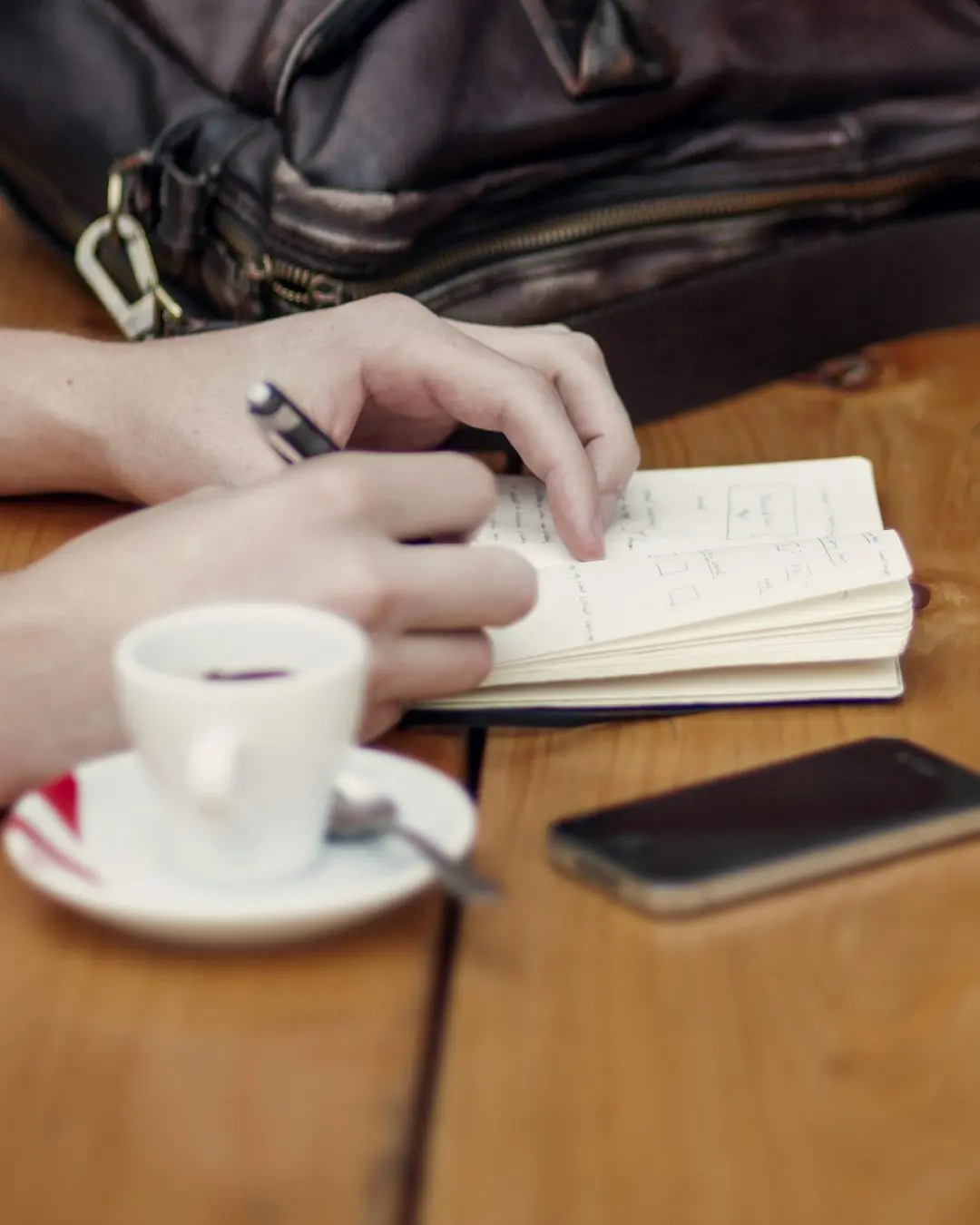 Deux personnes prennent des notes à une table en bois, une tablette et des cafés entre elles.